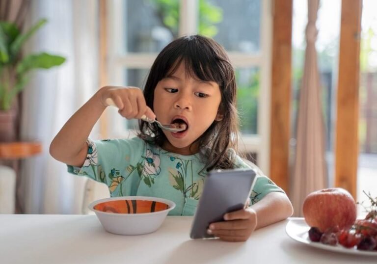 Criança comendo e utilizando o celular ao mesmo tempo.