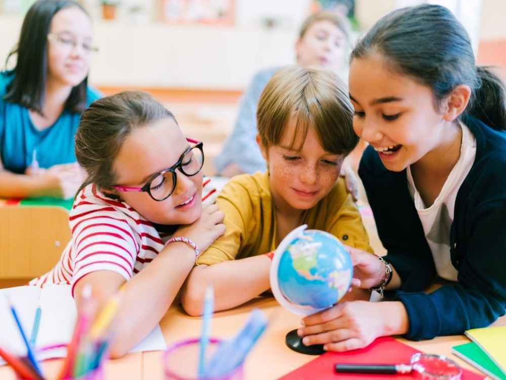 Alunos do Ensino Fundamental analisando um globo terrestre dentro da sala de aula