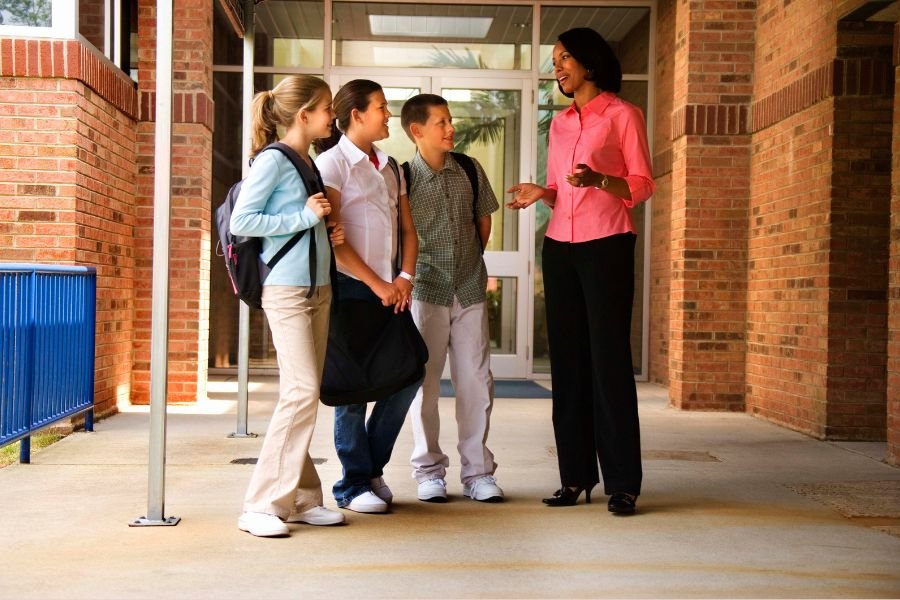 Estudantes adolescentes conversando com a professora no corredor da escola. Exemplo de educação emocional na escola.